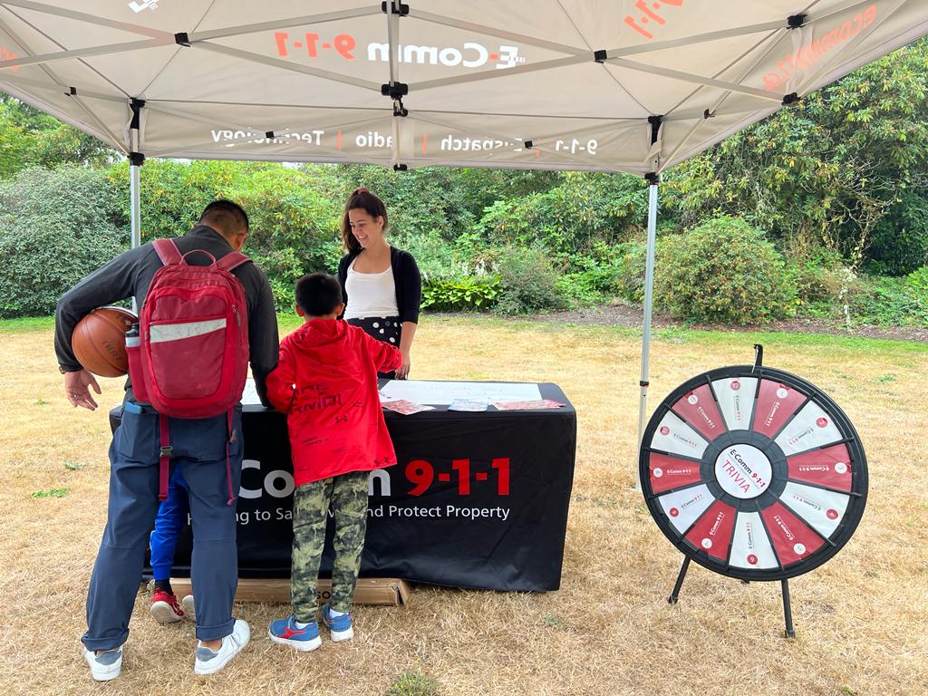 Communications Specialist Martina chatting with visitors at the Children's Safety Scavenger Hunt in Vancouver on August 26. A father is helping his son drawing a message for our 9-1-1 heroes on the poster boards.