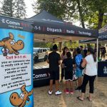 Communications Specialist Martina sharing important 9-1-1 info with visitors at the Abbotsford Police Movie Night on September 2. Communications Specialist Martina sharing important 9-1-1 info with visitors at the Abbotsford Police Movie Night on September 2. Several kids and a parent are lined up at the booth to spin E-Comm's trivia wheel and respond to a question about 9-1-1 and earn a 9-1-1 sticker.